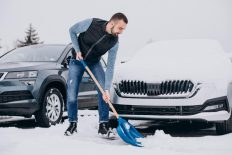 un homme qui pellete la neige pour illustrer le débat du service de déneigement d’hiver vs. abris d’hiver.